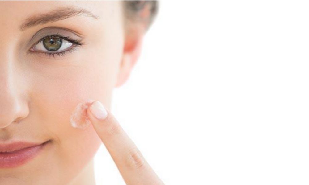 Caucasian female puts topical medication on acne blemish